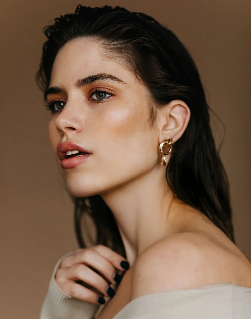 Close-up portrait of a woman with long dark hair, soft makeup, and a gold hoop earring, wearing an off-the-shoulder top. - Ear Reshaping in Orlando Park, IL